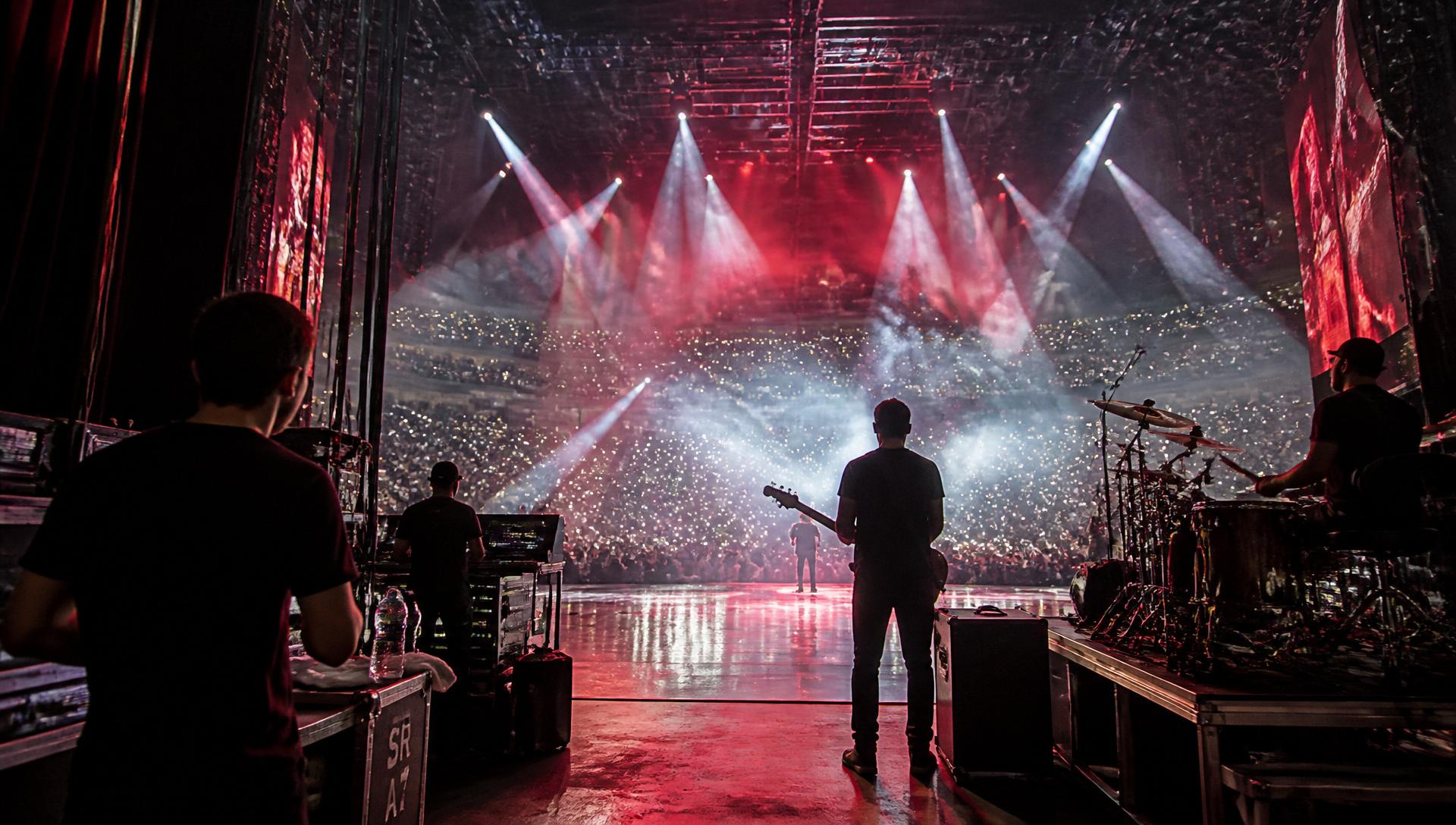 Backstage view of a large arena concert with spotlights and crowd flashlights