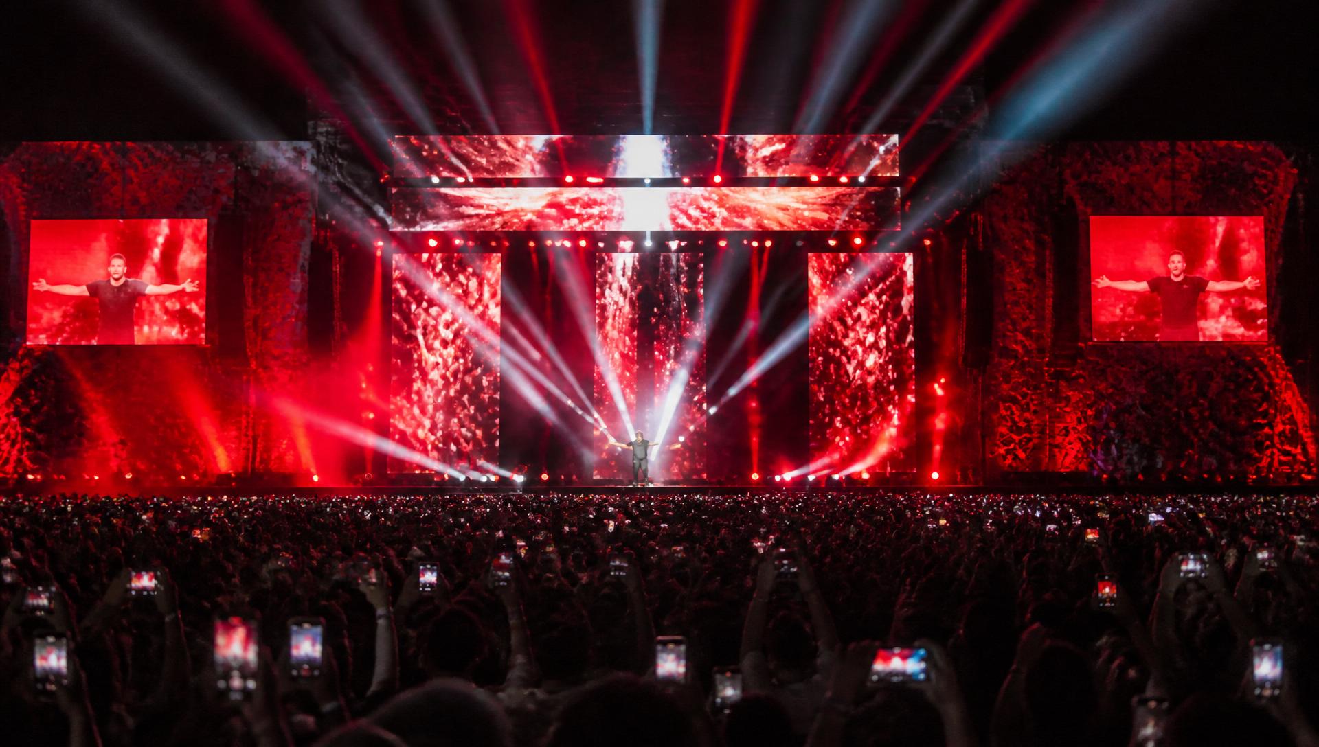Large-scale concert production with spotlights and a crowd holding up phone flashlights
